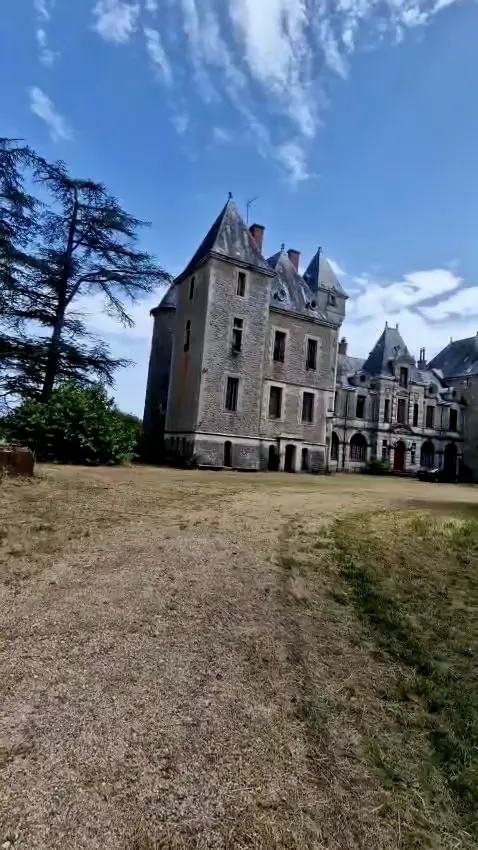 Le château vu depuis le parc, corps principal en pierre, tour carrée et toitures d’ardoise