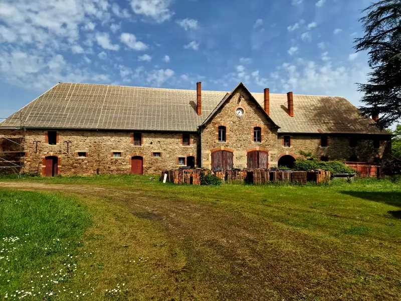 Les communs du château, longue façade en pierre à encadrements de brique, toiture d’un seul tenant
