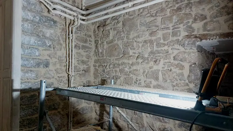 Échafaudage roulant dans une pièce en pierre, réseaux posés au plafond