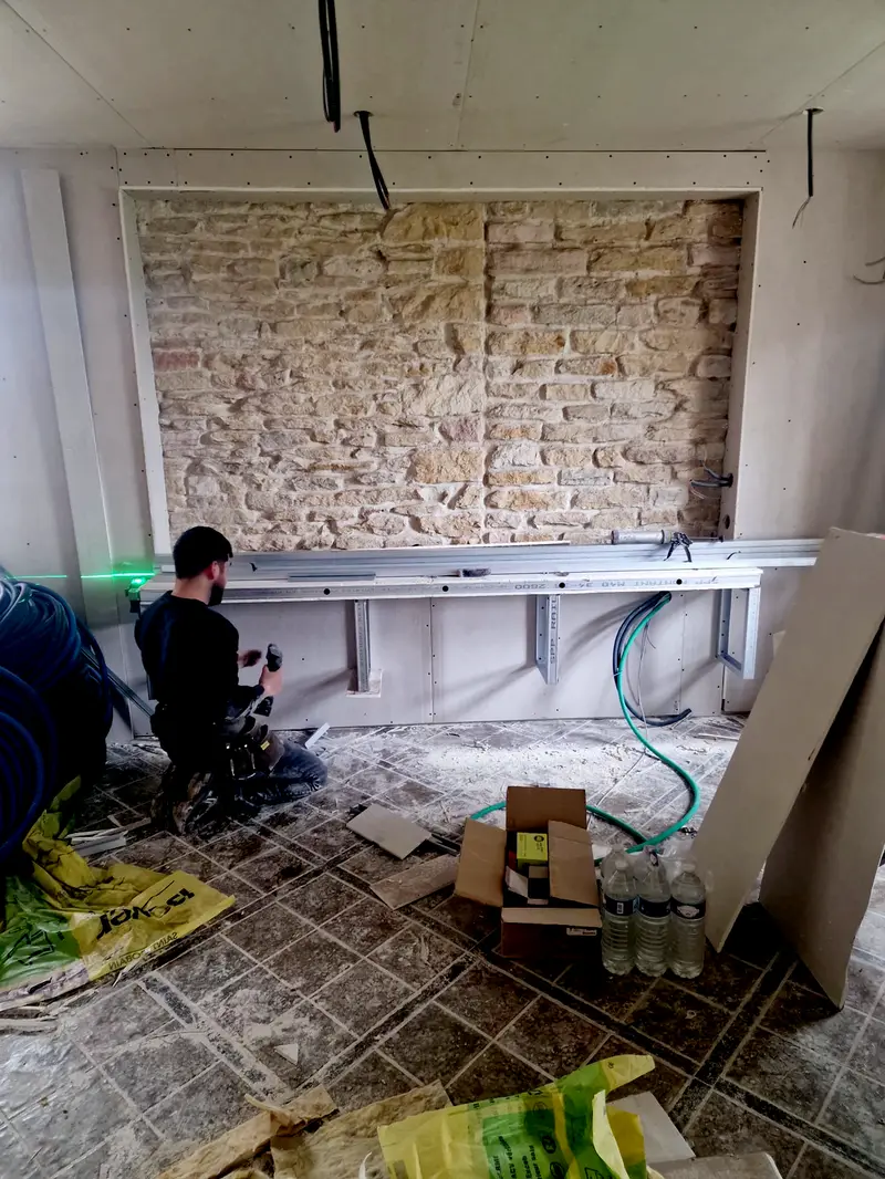 Doublage posé sur un mur en pierre, un compagnon règle l'ossature