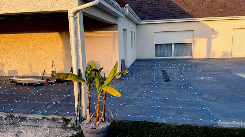 Terrasse en carrelage grand format en cours de pose le long d'un pavillon
