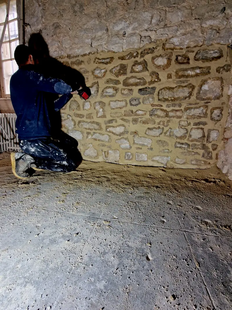 Un compagnon à genoux brosse les joints frais d'un mur en pierre repris à pierre vue