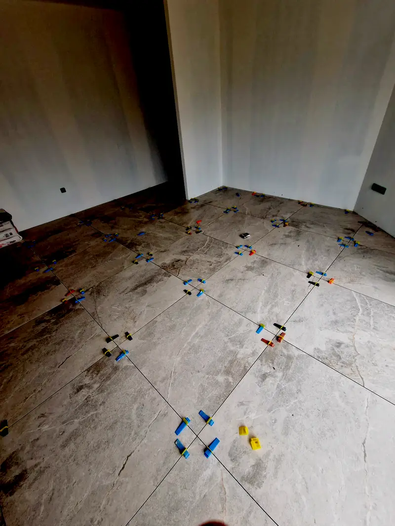 Carrelage grand format en cours de pose, croisillons de nivellement en place