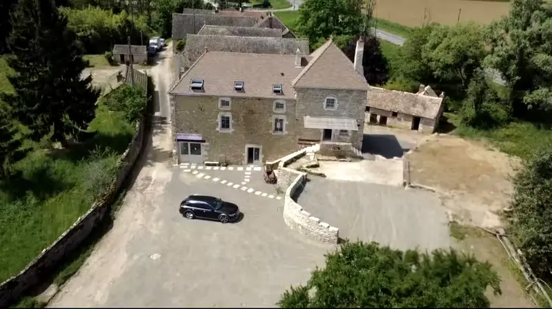 Le moulin vu du ciel, bâtiment principal en pierre, dépendances à droite, cour empierrée et muret courbe