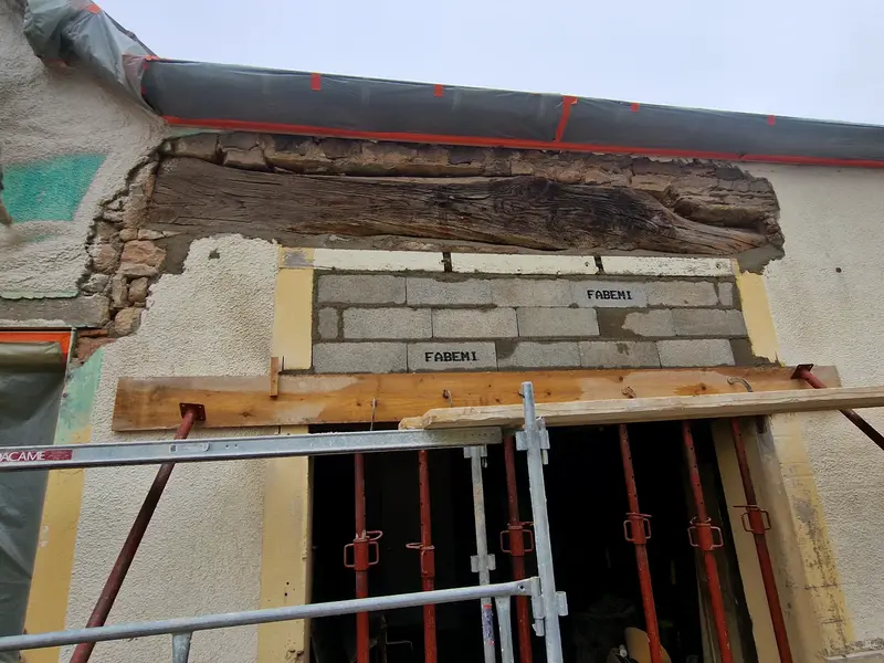 Façade reprise au-dessus d’une ouverture, ancien linteau bois déjointé, briques neuves montées, étai de bois en soutien