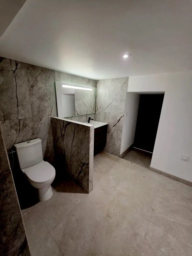 Salle de bains livrée, carrelage grand format effet marbre du sol au plafond, meuble vasque suspendu et miroir rétroéclairé